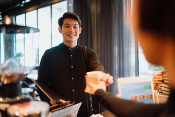 Asian customer takeing coffee cup from barista in cafe.