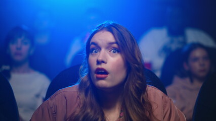 Young woman feeling angry with bad film. Upset girl looking smartphone in cinema