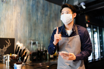 Asian barista man wearing mask taking order from customer in cafe.