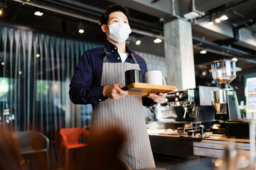 Asian barista man wearing mask serving coffee in cafe.