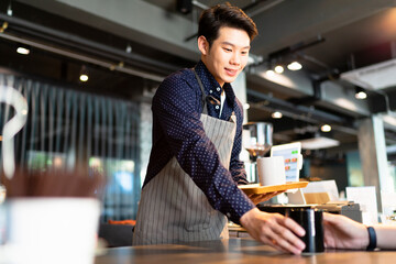 Asian waiter man serving hot coffee to customer in cafe.