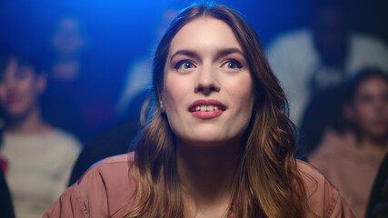 Fototapeta premium Happy woman watching movie in cinema. Cheerful girl eating popcorn on funny film