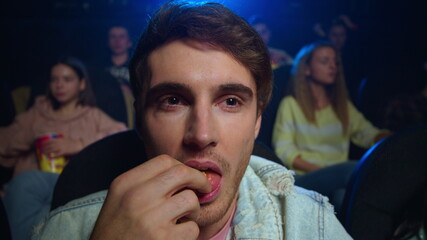 Cheerful man eating popcorn in cinema. Smiling guy looking comedy indoor.