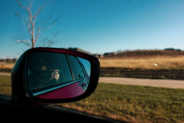 A person shooting photo through window of reflection in a sideview mirror of a car with motion blur nature countryside landscape during road trip vacation
