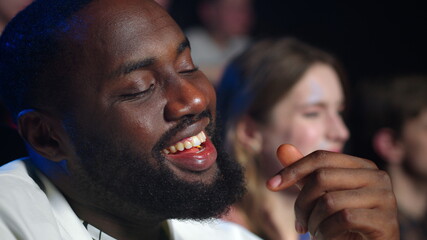 Happy african man laughing in cinema. Joyful afro guy eating popcorn in hall.