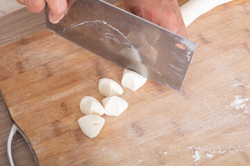 The chef cuts the long noodles on the cutting board into small doughs with a knife