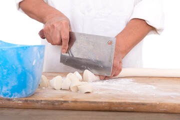 The pastry chef cuts the long white dough into small dough with a kitchen knife