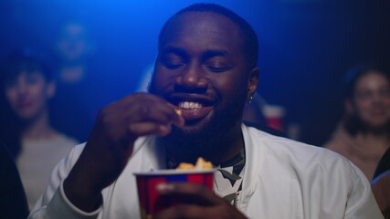 Cheerful african american man watching movie in cinema. Afro guy eating popcorn