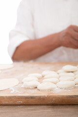 Small dough scattered on the cutting board and hands making dumplings in the background