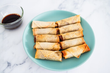 plant-based food, vegan homemade spring rolls with stir fried vegetables filling on blue plate next to soy sauce