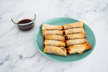 plant-based food, vegan homemade spring rolls with stir fried vegetables filling on blue plate next to soy sauce