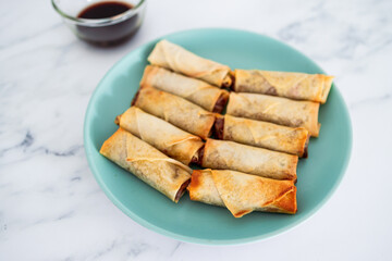 plant-based food, vegan homemade spring rolls with stir fried vegetables filling on blue plate next to soy sauce