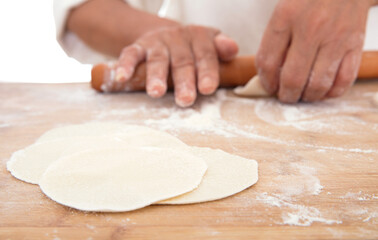 Chinese women roll dumpling wrappers on cutting board in kitchen