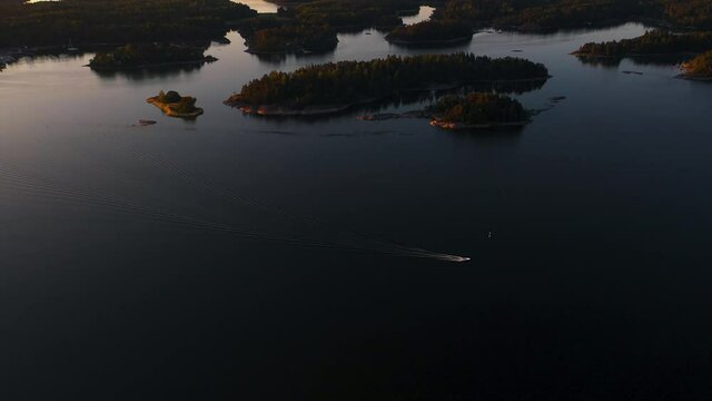 Aerial view following a boat, driving in middle of islands, in the Swedish archipelago, Baltic sea, in Sweden - reverse, tilt up, drone shot - serene, summer sunset,