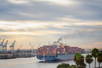 A huge freight container ship sailing into the ocean under dramatic sky emitting dark smoke of...