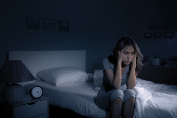 Depressed young Asian woman sitting in bed cannot sleep from insomnia..