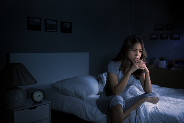 Depressed young Asian woman sitting in bed cannot sleep from insomnia..