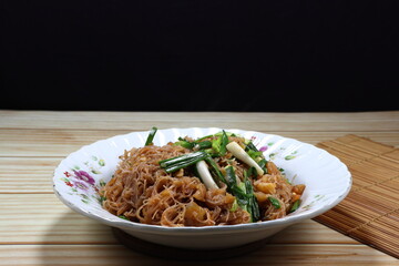 Fried and stirred spicy rice noodle mixed with local sauce and cutting spring onion serving on the plate. Famous traditional noodle menu in Asia restaurant. 