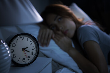Depressed young woman lying in bed cannot sleep from insomnia. Selective focus on alarm clock
