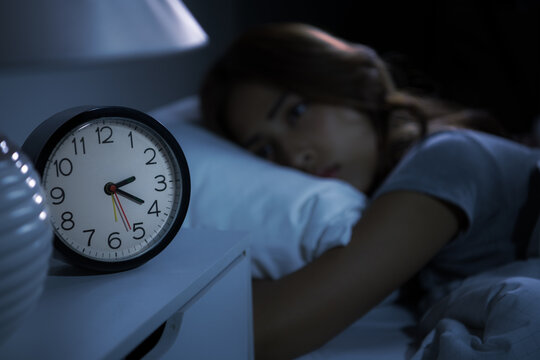 Depressed young woman lying in bed cannot sleep from insomnia. Selective focus on alarm clock
