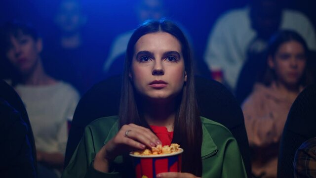 Young woman watching interesting movie in cinema. Attractive girl eating popcorn