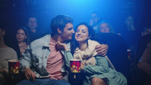 Happy couple watching movie in cinema. Happy man kissing woman in dark hall.