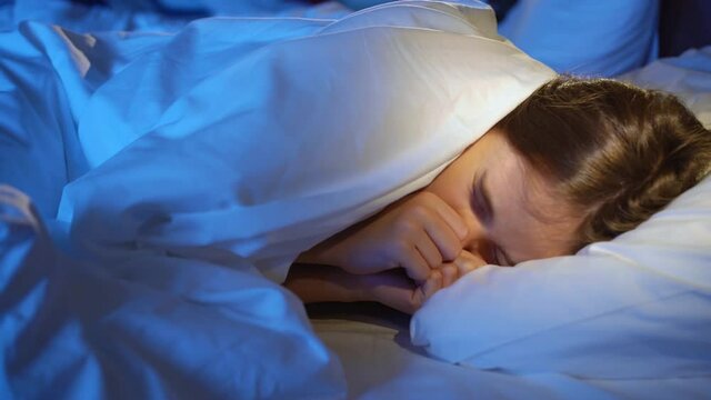 A girl naps in bed in her room, sees a nightmare and winces in her sleep.