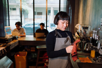 Asian woman barista cleaning glass cup behind the bar in cafe.