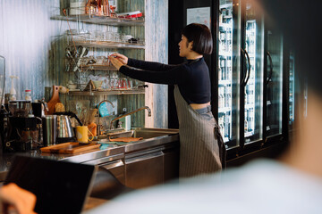 Barista woman working in cafe behind the bar.