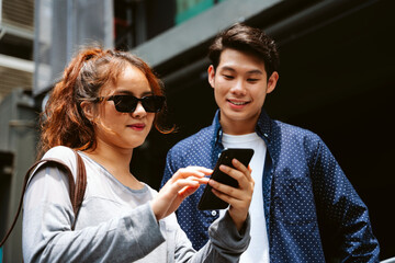 Asian couple tourists looking at digital map on smartphone.