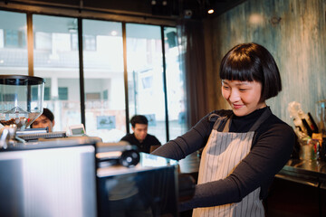 Asian woman working as barista making coffee for customer in cafeteria.