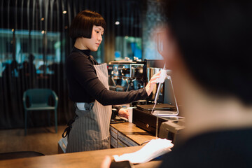 Short hair bartista woman serving hot coffee to customer at the bar.