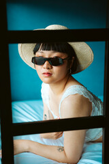 Portrait of asian short hair woman wearing sunglasses and hat on bed.