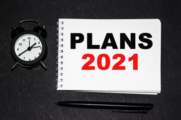 PLANS 2021 inscription on a white fragment. notebooks, watch and a pen on the table for information on a black background . A place for text. Business, marketing, financial concept