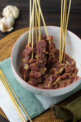 Preparation food to make Sate Daging or Indonesian popular Beef satay, beef slices marinated on ceramic white bowl, and some bamboo skewer. Beef satay usually make during Idul Adha celebration. 