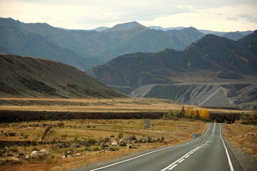 A straight two-lane asphalt road descends into a lowland surrounded by high, flat mountain peaks.