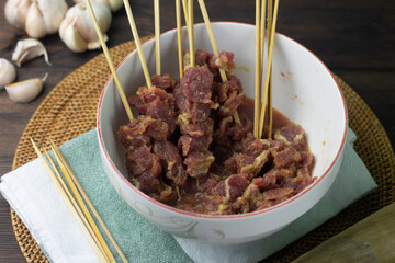 Preparation food to make Sate Daging or Indonesian popular Beef satay, beef slices marinated on ceramic white bowl, and some bamboo skewer. Beef satay usually make during Idul Adha celebration. 