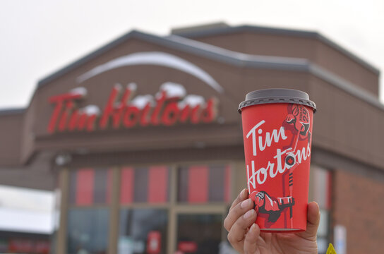Toronto, Ontario, Canada, 2020. Hand holding Tim Hortons coffee mug in from of the store. Tim Hortons is a famous fast food and coffee chain across the world but originally from Canada