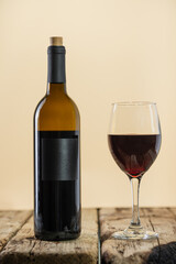 Macro shot of elegant bottle glass with fragrant red wine on beige background. Studio photo. Advertising and promotion. Space for text. Concept of alcoholic drinks.