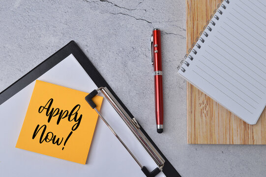 Top view of notebooks, pen, black file and memo note written with text APPLY NOW!. Business and education concept. 