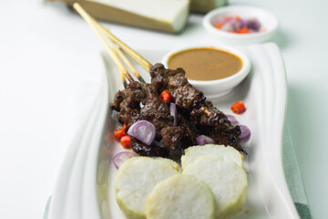 Sate Daging or Indonesian Beef Satay served on ceramic white plate, with slices of lontong, chilies, shallot and peanut sauce. Usually served on Idul Adha celebration. Isolated white background.  