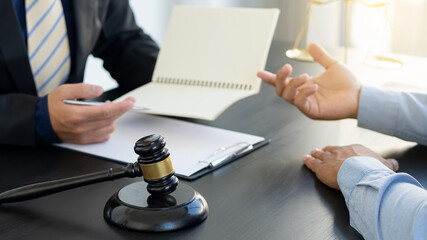 Lawyer hammer placed in front of male businessman and male lawyer or judge advisor, having a team meeting with clients, legal concept with gold scales as background.