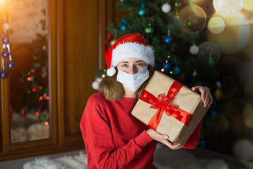 Obraz na płótnie Canvas girl in red clothes and medical mask unfold New year gifts. the concept of celebrating Christmas midnight. Holiday's decor boce, Christmas tree