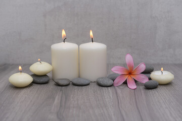 Obraz na płótnie Canvas Spa setting with plumeria flowers, five candles and gray stones on wood background 