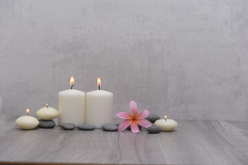 Spa setting with plumeria flowers, five candles and gray stones and on wood background
 