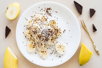 Low calorie dessert. Banana, chocolate and coconut flakes on white plate.