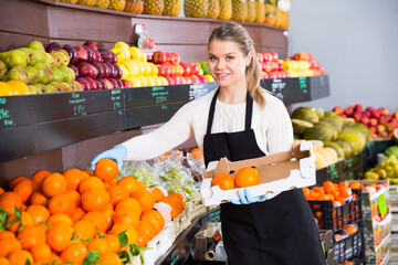Obraz premium Portrait of young female seller lays out fruits of the box on the supermarket