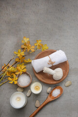Fototapeta na wymiar Concept for spa salon, with yellow orchid and white bath towel and herbal ball, in wooden bowl and candle,stone,salt in spoon and bamboo on gray background, Copy space 