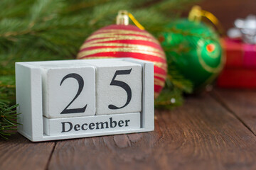 December 25 on a white wooden calendar on a wooden background next to the Christmas tree.The concept of Christmas.