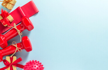 Fitness concept happy Christmas and a happy New year. Red dumbbells, fitness elastic band, massage ball and Golden gifts with red ribbons on a blue background. Flat lay, top view, copy space